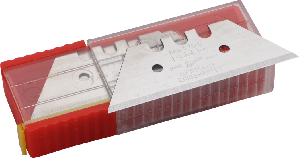 Gros plan d'une boîte de lames de rechange pour cutter dans un distributeur en plastique rouge avec un couvercle coulissant transparent. Une lame métallique à pointe triangulaire est partiellement sortie et repose sur la boîte ; la surface de la lame porte des marquages gravés, notamment 'No.570E' et 'GERMANY EISGEHÄRTET'. Le distributeur rouge présente une surface striée et un capuchon d'extrémité jaune. La photo, sur fond blanc et éclairage uniforme, met en évidence les textures métalliques et le tranchant fin.