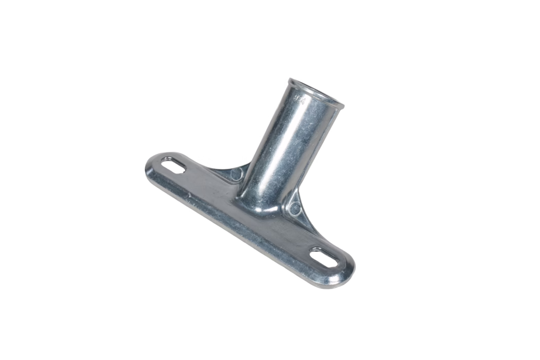 Close-up of a zinc-plated angled metal mounting bracket. The component features a flat rectangular base with two elongated oval mounting slots and a welded cylindrical sleeve set at an angle to the base. The surface has a bright, slightly textured galvanized finish with minor tool marks and a small stamped marking near the sleeve. Reinforcing ribs are formed where the sleeve meets the base, and rounded edges and countersunk areas are visible for fastener clearance. The bracket is photographed on a white background and is clearly intended to accept a tubular rod or pole and be secured with screws or bolts through the slotted holes.