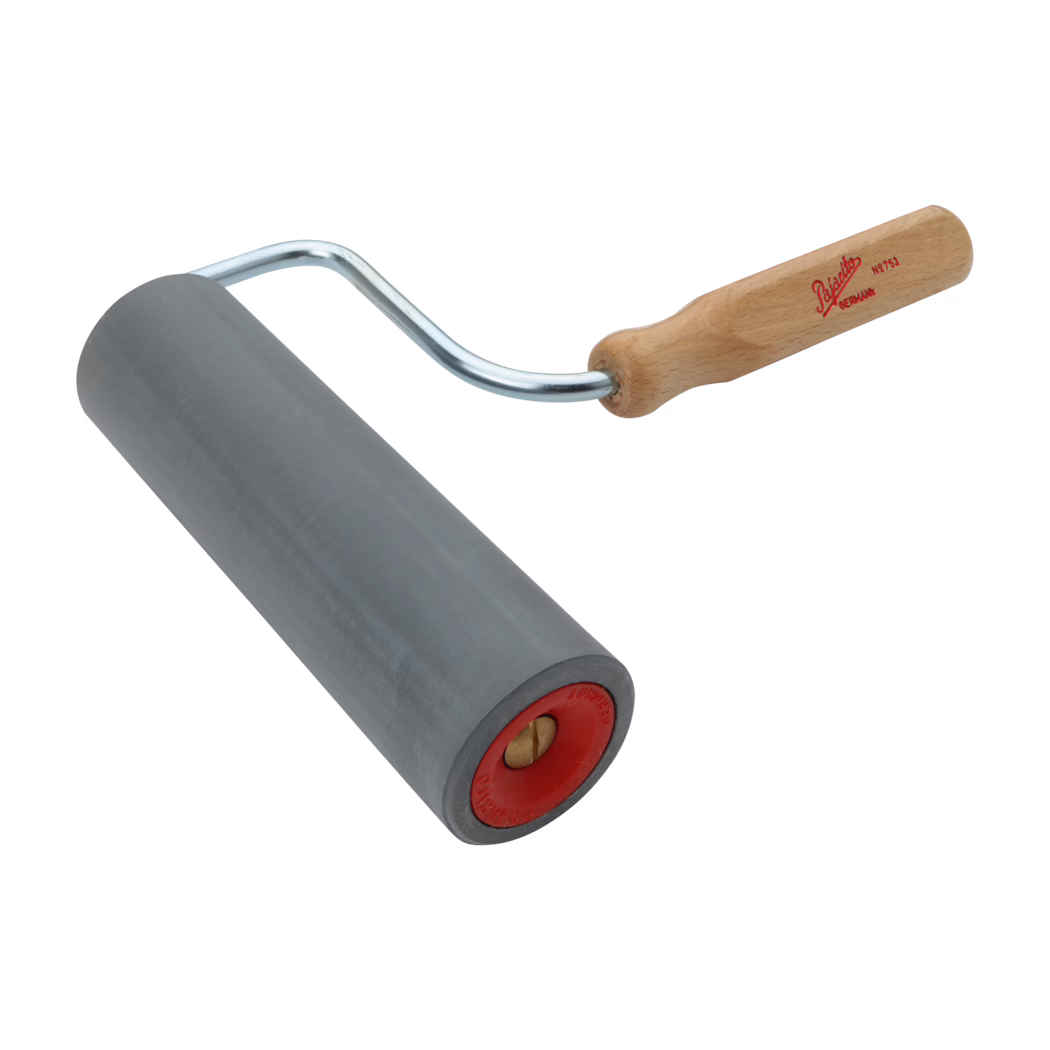 Pajarito_Dummy_Pressure roller foam rubber_034552_2021-02 A hand tool composed of a smooth, cylindrical gray rubber roller mounted on a bent metal frame with a light wooden handle bearing a red logo. The roller shows a red plastic end cap with a visible brass axle. Photographed on a white background from an angled perspective, the tool is typically used for smoothing wallpaper, laminates or pressing down materials.