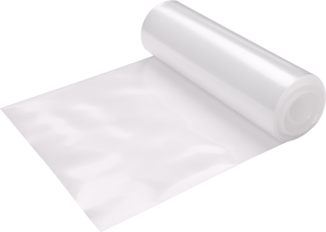 Pajarito_Dummy_Downpipe foil_021517_2021-02 A large roll of transparent glossy plastic film partially unrolled on a clean white background. The film appears clear with a slight milky sheen and a smooth reflective surface showing soft highlights; it is wound around a cylindrical core positioned at the top right of the image, with a flat sheet extending diagonally across the frame. The material looks like flexible polyethylene used for packaging, protective covering, vacuum sealing or food storage, and the photo emphasizes the texture, sheen and thin, flexible nature of the sheet.