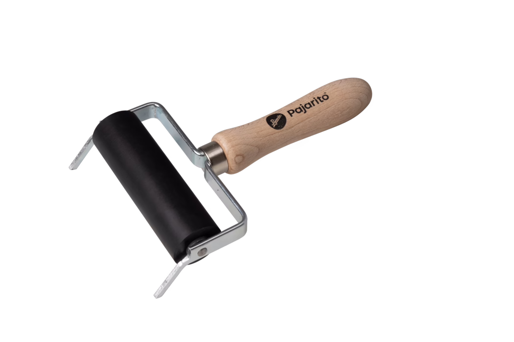 Un petit brayer (rouleau d'encrage) photographié sur fond blanc. Il possède un rouleau en caoutchouc noir lisse monté sur un châssis métallique coudé argenté et un manche ergonomique en bois clair imprimé du nom de la marque « Pajarito ». Le châssis métallique fixe le rouleau par des rivets visibles ; le manche en bois présente le veinage naturel et une extrémité arrondie. L'outil sert à répartir uniformément l'encre ou la peinture sur des plaques d'impression, du linoléum ou du papier et semble propre et inutilisé. La composition est légèrement diagonale, le rouleau en bas à gauche et le manche s'étendant vers le coin supérieur droit.