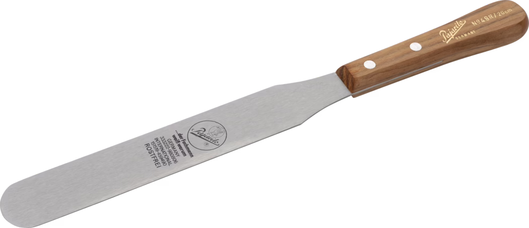 Pajarito_Dummy_Colour knife _036121_2021-02 Spatule/palette en acier inoxydable avec une longue lame étroite brossée et une pointe arrondie, conçue pour étaler, soulever et lisser des aliments délicats comme le glaçage de gâteaux. La lame est marquée d'un logo circulaire et d'inscriptions techniques incluant « Germany » et « ROSTFREI » ; elle se rétrécit pour rejoindre une mitre pleine qui se fixe à un manche en bois poli maintenu par deux rivets métalliques. Le manche présente une forme ergonomique légèrement effilée avec un marquage de marque doré, la longueur de la lame est d'environ 20 cm (n° 491), ce qui en fait un outil solide, bien équilibré et adapté aux travaux de précision en pâtisserie.