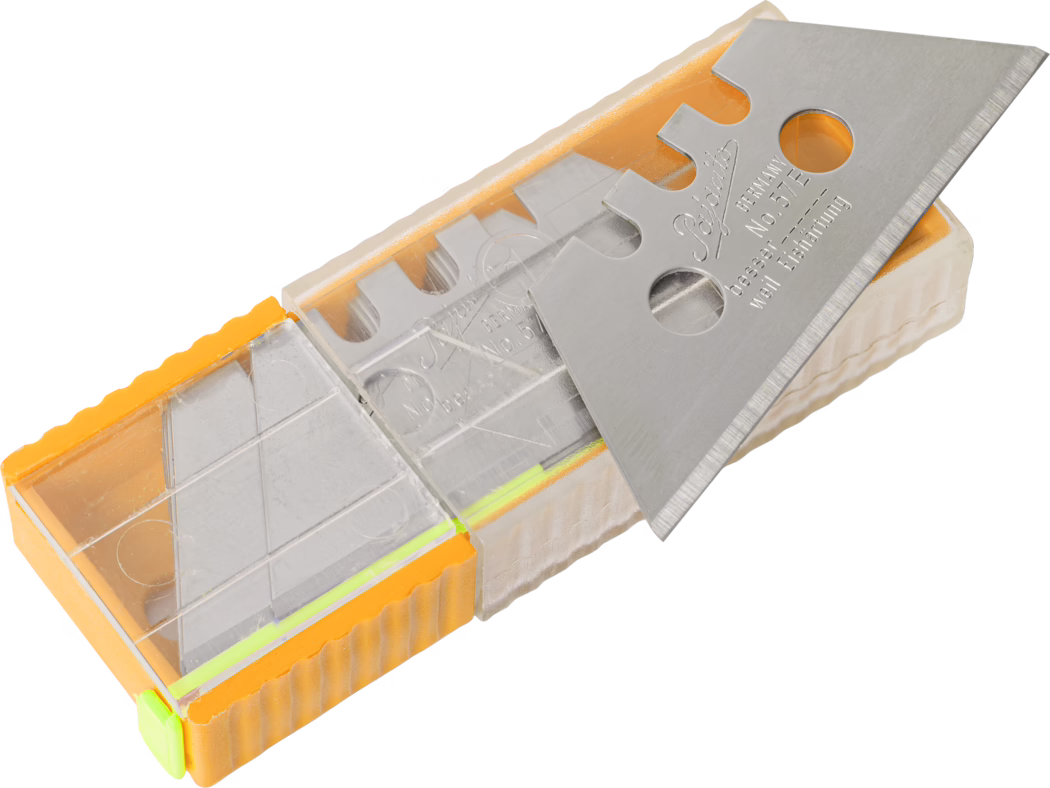 Une boîte en plastique contenant plusieurs lames triangulaires de cutter. Le boîtier transparent et orange contient des lames empilées en acier inoxydable avec des encoches et des trous ronds ; une lame est posée sur le dessus et montre le tranchant biseauté et un marquage gravé. L'image est bien éclairée sur un fond blanc neutre et met en évidence la texture du boîtier en plastique et les surfaces métalliques réfléchissantes en gros plan, légèrement inclinées.
