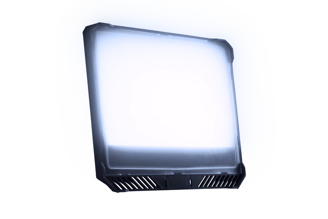 Panneau LED rectangulaire légèrement incliné avec un cadre en plastique foncé et un diffuseur dépoli émettant une lueur blanc-bleutée ; le bord inférieur présente des fentes d'aération inclinées et des encoches de fixation. L'élément est isolé sur fond blanc, avec de subtils reflets sur la surface et un doux halo lumineux.