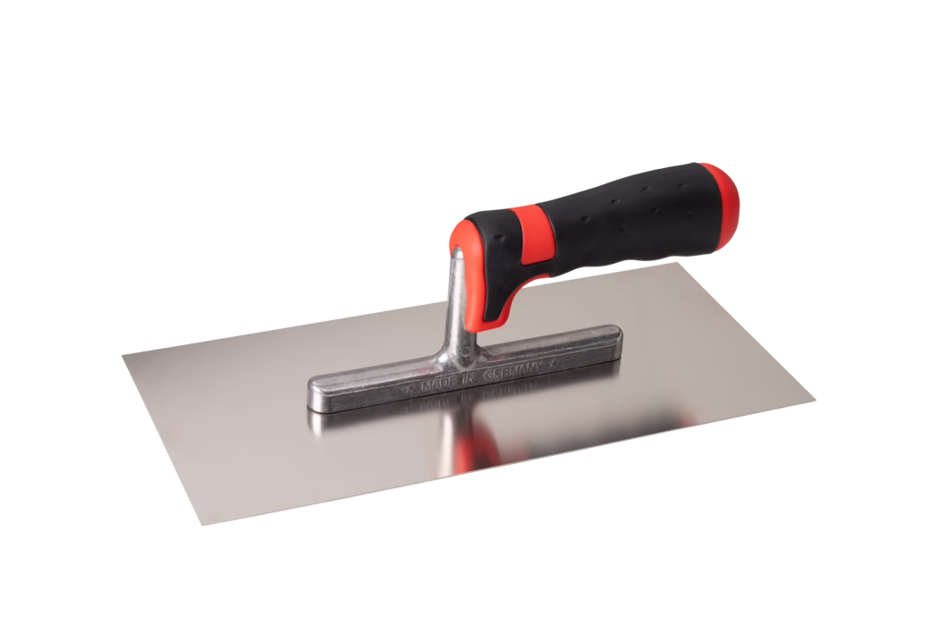 Pajarito_Dummy_Trowel soft handle Performance Line_034664_2021-02 Truelle rectangulaire en acier inoxydable avec une lame plate et lisse et un court fût métallique soutenant une poignée ergonomique noire et rouge à prise souple. La lame polie est réfléchissante et présente une faible réflexion de la poignée ; le fût métallique est estampillé MADE IN GERMANY. La poignée comporte des accents rouges à l'avant et à l'arrière et une surface en caoutchouc texturée pour une bonne prise. L'outil est photographié isolé sur fond blanc, en léger contre-plongée latérale. Convient pour appliquer et lisser le mortier, l'enduit ou le plâtre.