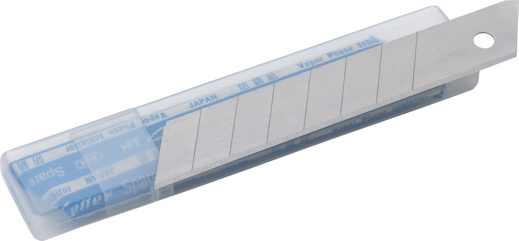 Un étui transparent en plastique contenant une lame de rechange segmentée pour cutter à dégagement par cassure. La lame en acier argenté est partiellement avancée et présente plusieurs segments pré-découpés pour être cassés ; un segment est biseauté et exposé. Un papier protecteur bleu à l'intérieur porte les inscriptions 'JAPAN' et 'Vapor Phase Inhibitor'. Le bras métallique de la lame est estampillé 'NT JAPAN' et comporte un trou rond à l'extrémité. L'étui est posé en diagonale sur un fond blanc.